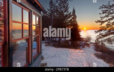 Ländliche Landschaft, Sonnenaufgang im Winter und Reflexionen in den Kabinenfenstern entlang der Nordküste des Lake Superior im Norden Minnesotas Stockfoto