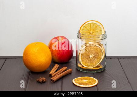 Frischer Apfel und Orange, Zimtstangen und getrocknete Orangenscheiben in einem Glasgefäß. Speicherplatz kopieren. Dunkler Holz- und weißer Hintergrund. Stockfoto