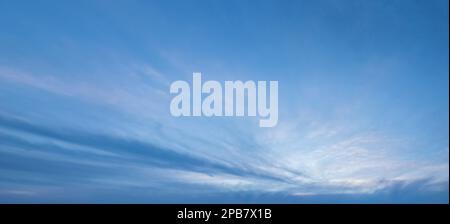 Weiße, federnde Wolken mit Zirrusschichten in einem blauen Himmel, Panoramafoto des blauen bewölkten Himmels bei Sonnenuntergang Stockfoto