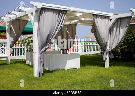 Pavillon aus weißem Segeltuch mit Gartenmöbeln aus Kunststoff in einem grünen Sommerrasen. Stockfoto