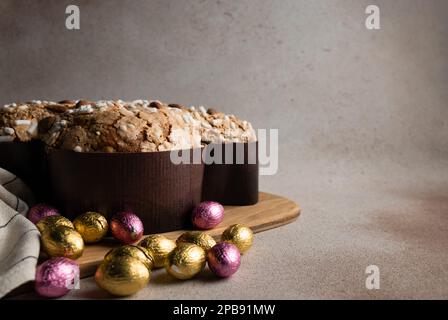 Ostertaubenkuchen mit Schokolade Ostereier in Folie auf Holzbrett gewickelt, gestreifte Serviette auf Betonhintergrund, Kopierbereich Stockfoto