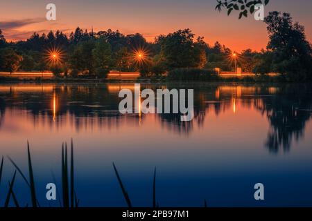 Wunderschöner Sonnenuntergang am Goettinger Kiessee. Mit Lichtspuren von Autos und Lichtsternen von Laternen Stockfoto