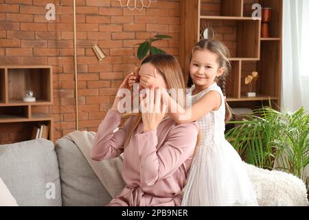 Süßes kleines Mädchen, das zu Hause die Augen seiner Mutter schließt Stockfoto