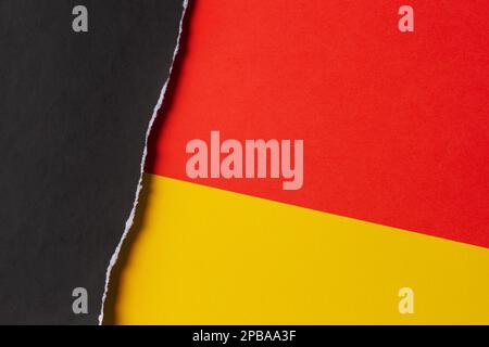 Schwarzer Grunge gerissenes Papierstück mit zerkleinerter Kante auf gelbem und rotem Papierhintergrund. Draufsicht, Kopierbereich Stockfoto