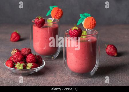 Erdbeer-Smoothie mit Joghurt und Eiswürfeln in zwei Gläsern auf einem braunen Tisch Stockfoto