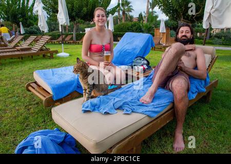 08-09-2015 Paphos, Zypern. Touristen (junge Leute) trinken Bier auf Liegen an einem Strand mit Gras aus den Niederlanden in Paphos in einer 5-Sterne-Hure Stockfoto