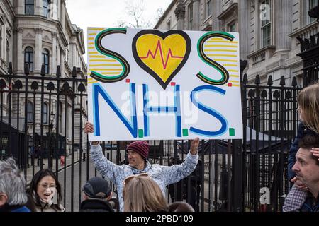 Mann hält die "SOS NHS" Plakette vor der 10 Downing Street während der NHS-Demonstration, gingen NHS-Arbeiter durch London, März 2023 in London. Stockfoto