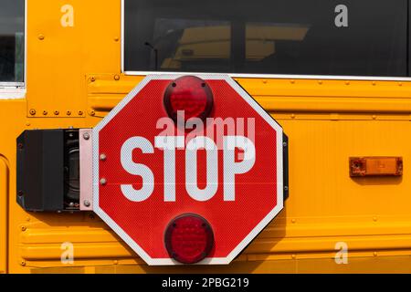 Ein großes rotes Stoppschild neben einem gelben Schulbus. Stockfoto