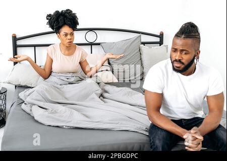 Streit, Meinungsverschiedenheiten, Eifersucht. Ein afroamerikanisches Ehepaar regelt zu Hause im Schlafzimmer Dinge, eine Frau schreit einen Mann an, beschuldigt ihn. Missverständnisse in Beziehungen, Streit Stockfoto