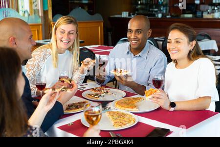 Fröhliche junge Erwachsene genießen Pizza im gemütlichen Restaurant Stockfoto