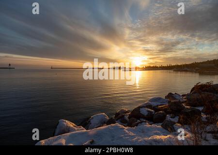 Ein wunderschöner Sonnenuntergang auf dem Lake Superior im Grand Marais Minnesota erhellt den Winterhimmel in Farbe, wenn die Wolken ihn setzen Stockfoto