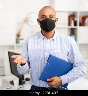 Geschäftsmann in Schutzmaske macht Notizen in Dokument Stockfoto