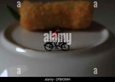 Eine Miniaturfigur eines Radfahrers, der neben dem Kuchen und auf dem Teller fährt. Stockfoto