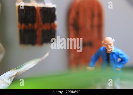 Miniaturfigur eines Großvaters, der vor dem Haus wartet. Stockfoto