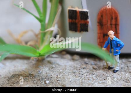 Miniaturfigur eines Großvaters, der vor dem Haus wartet. Stockfoto