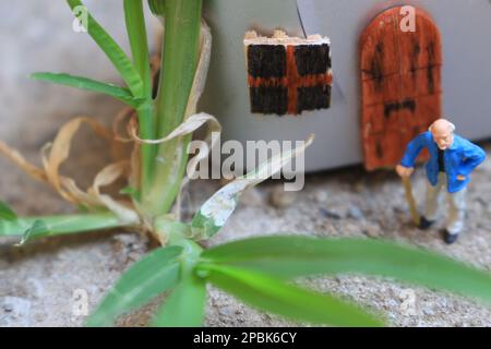 Miniaturfigur eines Großvaters, der vor dem Haus wartet. Stockfoto