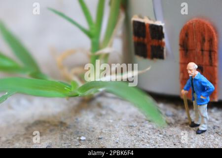 Miniaturfigur eines Großvaters, der vor dem Haus wartet. Stockfoto