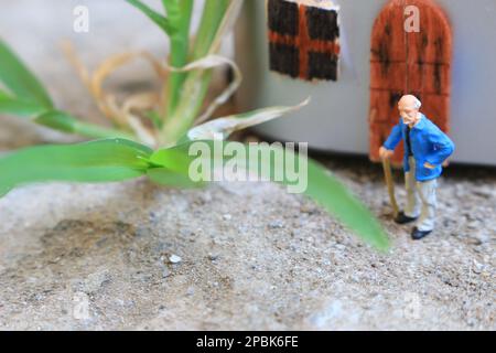 Miniaturfigur eines Großvaters, der vor dem Haus wartet. Stockfoto