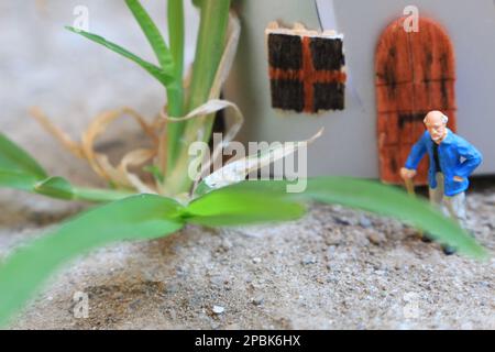 Miniaturfigur eines Großvaters, der vor dem Haus wartet. Stockfoto
