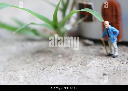 Miniaturfigur eines Großvaters, der vor dem Haus wartet. Stockfoto