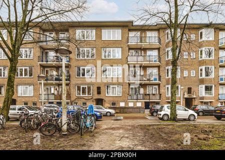 Ein Apartmentkomplex mit Fahrrädern, die in der Einfahrt geparkt sind, und Autos, die auf der Seite der Straße daneben geparkt sind Stockfoto