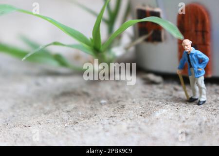 Miniaturfigur eines Großvaters, der vor dem Haus wartet. Stockfoto