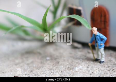 Miniaturfigur eines Großvaters, der vor dem Haus wartet. Stockfoto