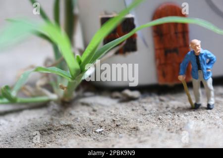 Miniaturfigur eines Großvaters, der vor dem Haus wartet. Stockfoto