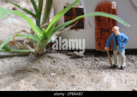 Miniaturfigur eines Großvaters, der vor dem Haus wartet. Stockfoto