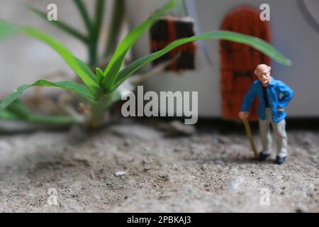 Miniaturfigur eines Großvaters, der vor dem Haus wartet. Stockfoto