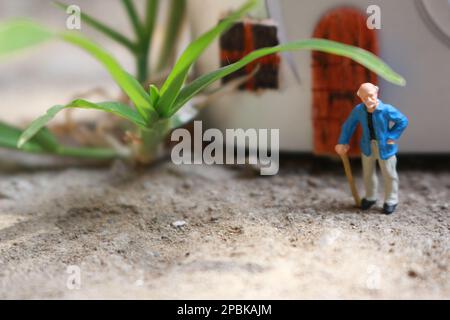Miniaturfigur eines Großvaters, der vor dem Haus wartet. Stockfoto