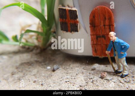 Miniaturfigur eines Großvaters, der vor dem Haus wartet. Stockfoto