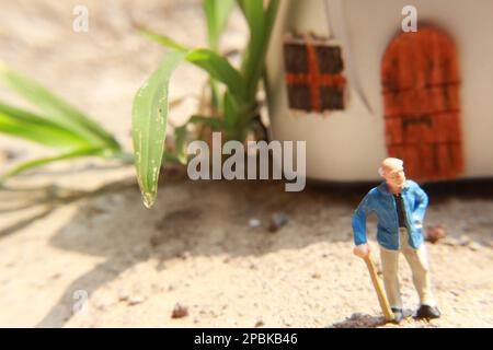 Miniaturfigur eines Großvaters, der vor dem Haus wartet. Stockfoto