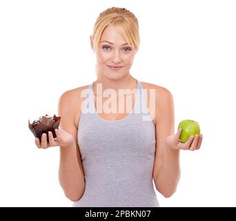 Manchmal ist es schwierig, die gesunde Wahl zu treffen. Eine junge Frau, die zwischen einem Muffin und einem Apfel wählen muss. Stockfoto