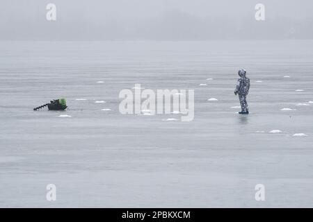 Angelausrüstung und ein Fischer in warmer Kleidung auf dem dünnen Quelleis des Voronesch-Reservoirs. Jedes Jahr nehmen verzweifelte Liebhaber des Winterfischens das Eis des Voronesch-Reservoirs. Die Fischer werden nicht durch ein Auftauen oder sogar das Eintreffen des Frühlings aufgehalten. Die Aufregung treibt diese Menschen auf dünnem und manchmal verschwommenem Eis an, was zu Spannungen für den Dienst der Stadt führt. Rettungskräfte und Polizisten entfernen Fischer aus Eisschollen und fischen sie aus Gully, während medizinische Arbeiter um das Leben von Menschen kämpfen, die ertrinken oder kalt sind. Stockfoto