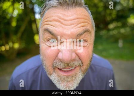 Ein bärtiger Mann, der in die Linse blickt und in einem Nahaufnahme-Kopfschuss draußen schielt Stockfoto