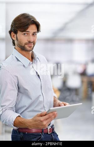 Er ist ein selbstbewusster junger Geschäftsmann. Porträt eines gutaussehenden jungen Geschäftsmanns, der in seinem Büro mit einem Tablet steht. Stockfoto