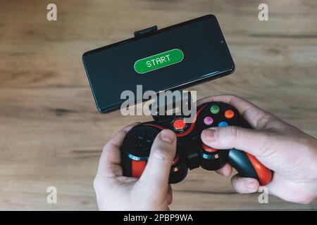 Hände mit Joystick und Telefon. Ein Gamer spielt auf einem Smartphone Stockfoto