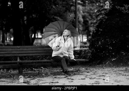 Eine Frau sitzt bei Regen auf einer Parkbank. Schwarzweißfoto. Stockfoto