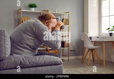 Trauriger, trauernder Seniorenmann mit Stock sitzt zu Hause auf der Couch und weint Stockfoto