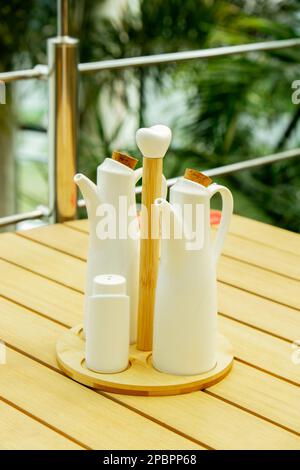 Restaurant im Hotel mit Tischen und niedlicher Dekoration, salter. Salz- und Pfefferstreuer auf dem Tisch im Café. Grüner Hintergrund. Garset Olivenöl, Salz, Pfeffer, Gewürze und Zahnstocher. Grüne Pflanzen auf dem Hintergrund Stockfoto