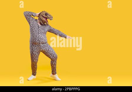 Lustiger Fettsack in unsinniger Dino-Maske und im Leopardenanzug isoliert auf orangefarbenem Hintergrund. Stockfoto