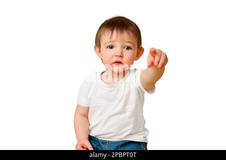 Porträt eines aufgewühlten Kleinkindes im Studio isoliert auf weißem Hintergrund. Das beleidigte Kind zeigt mit dem Zeigefinger in einem weißen T-Shirt und blauem jea nach vorne Stockfoto