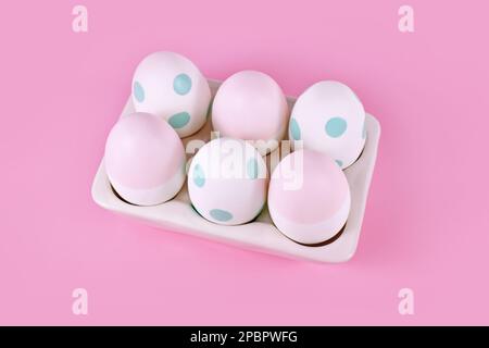 Pastellfarbene, bemalte Ostereier auf einem Eiertablett auf pinkfarbenem Hintergrund Stockfoto