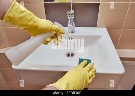 Putz in der öffentlichen Toilette des Cafés, männliche Hand in gelben Handschuhen wischte das Waschbecken mit einem Schwamm Stockfoto