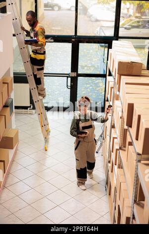 Der Supervisor scannt Kartons mit dem Scanner des Stores während der Lagerbestandsaufnahme und gibt den Barcode der Produkte auf dem Tablet-Computer ein. Mitarbeiter im Schutzbereich bereitet Kundenbestellungen im Lager vor Stockfoto