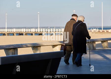 Ein älteres Paar, das an der Strandpromenade entlang spaziert Stockfoto