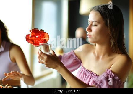 Frau, die Glas mit Wasser füllte, sitzt in einem Restaurant Stockfoto