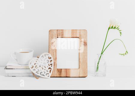 Bilderrahmen aus Holz, Bücher, Kaffeetasse, geschnitztes Dekorherz und Freesia-Blumen in Vase auf weißem Tisch. Speicherplatz kopieren. Stockfoto