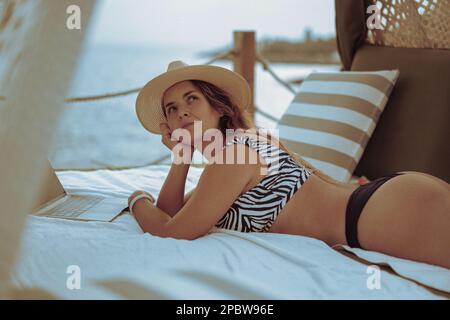 Frau, die im Urlaub an einem Laptop arbeitet, am Strand, Freiberufler. Stockfoto